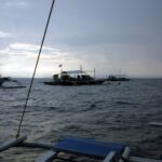 Trzy nurkowe łodzie banca na kotwicy na Monad Shoal pod szarym porannym niebem, widziane z pokładu innej łodzi