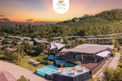 Kalima Resort Khao Lak z lotu ptaka o zachodzie słońca, z basenami i łukowatymi dachami u stóp zalesionego wzgórza
