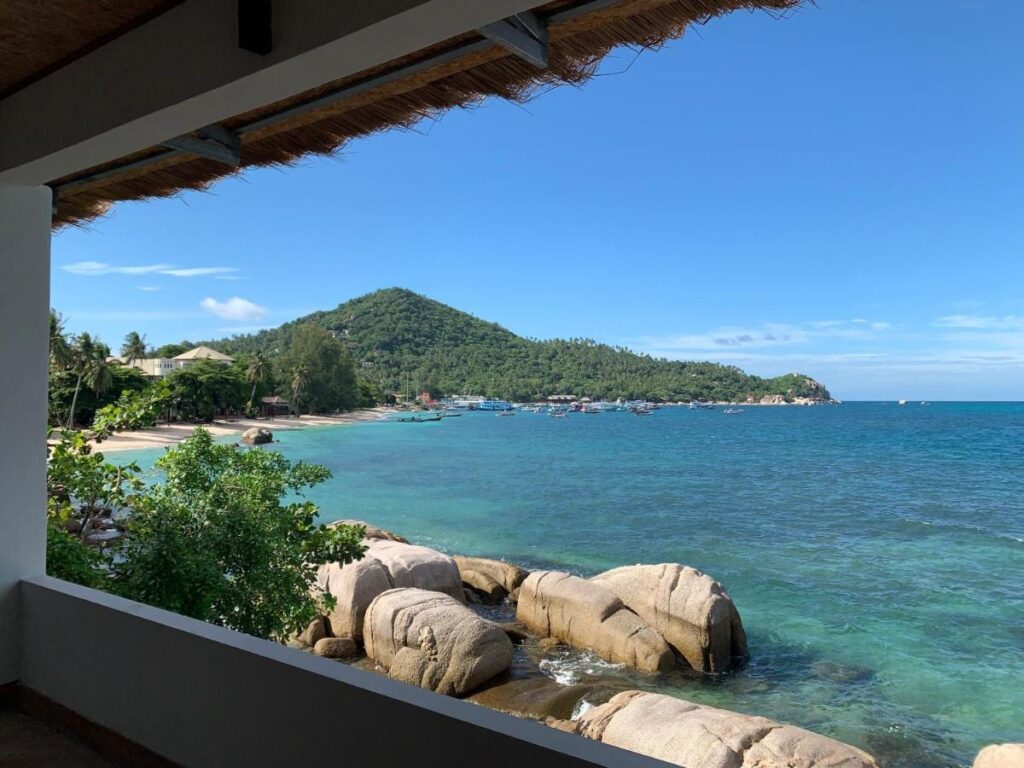 Zatoka ze skałami i zakotwiczonymi łodziami, widziana z zadaszonego tarasu Koh Tao Heritage