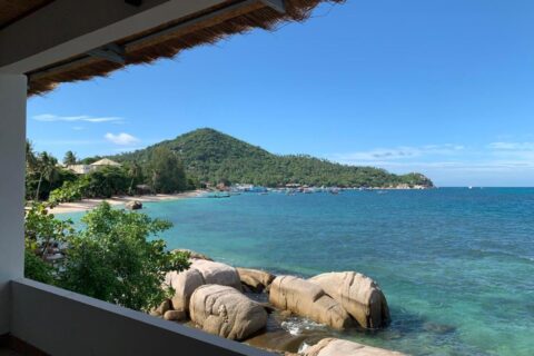 Zatoka ze skałami i zakotwiczonymi łodziami, widziana z zadaszonego tarasu Koh Tao Heritage