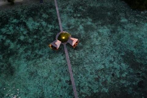 Nocny widok z lotu ptaka na długi drewniany pomost biegnący od plaży, z dwiema chatkami na palach w połowie drogi