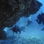 Czterech nurków wypływa z koralowego tunelu nad piaszczystym dnem na Cozumel, ze skalnym sklepieniem nad nimi