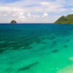 Widok z lotu ptaka na długą plażę Diamant nad turkusową wodą, Rocher du Diamant w oddali na morzu i Morne Larcher, zielone wzgórze, po prawej